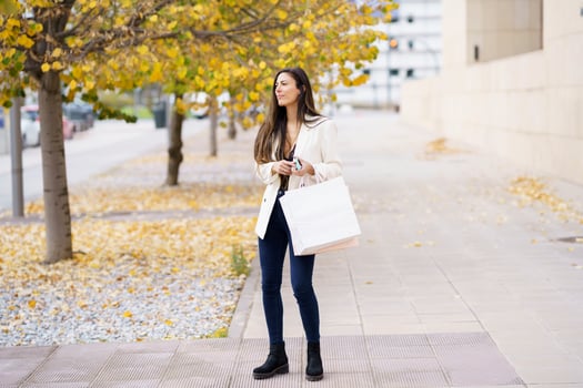 A young woman leisurely strolling down a beautiful autumn street, holding a shopping bag photo