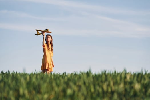 Holding toy plane. Happy girl have a walk outdoors on the field at summer photo