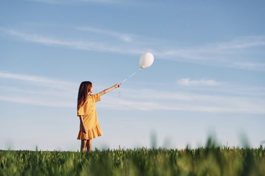 Holding balloon in hand. Happy girl have a walk outdoors on the field at summer.. photo