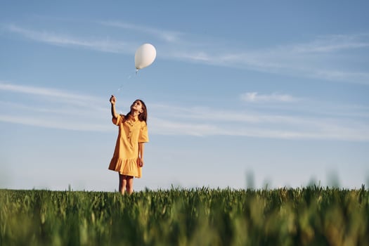 Holding balloon in hand. Happy girl have a walk outdoors on the field at summer., photo