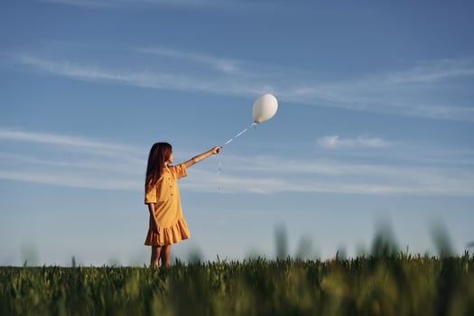 Holding balloon in hand. Happy girl have a walk outdoors on the field at summer. photo