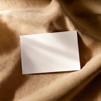 A blank white business card with soft shadows, placed on a smooth beige linen fabric photo