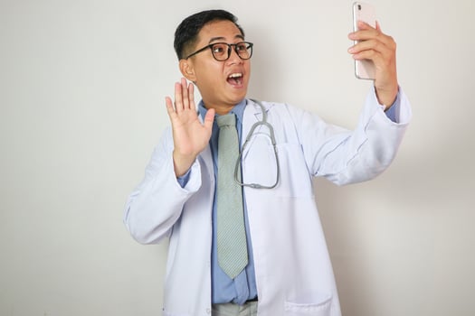 Asian male doctor talking and looking to camera in conference ,Positive doctor waving and having online consultation on digital smartphone photo