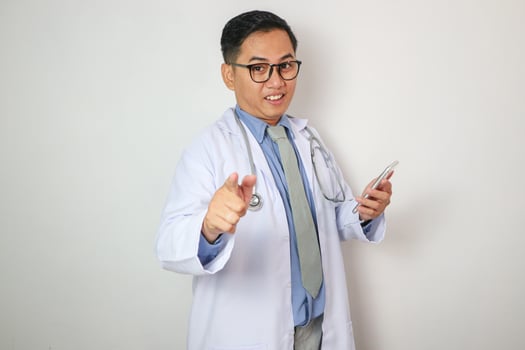 healthcare, profession and medicine concept - happy smiling indian doctor or male nurse in blue uniform with clipboard and stethoscope pointing finger to camera over white background photo