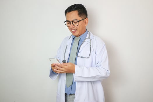 Good looking Indian male doctor using speaking over or presenting Smartphone, standing isolated over white background. photo