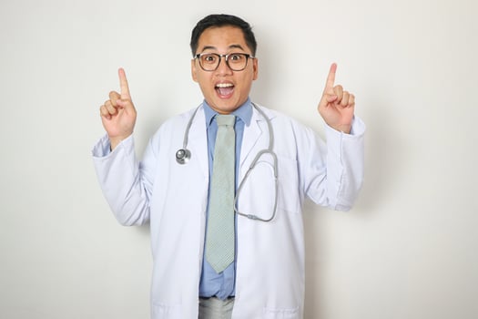 Surprised glad attractive mature asian doctor in white coat, glasses with stethoscope showing finger up on empty space isolated on white background. Therapist got idea, treatment, great offer and ad photo