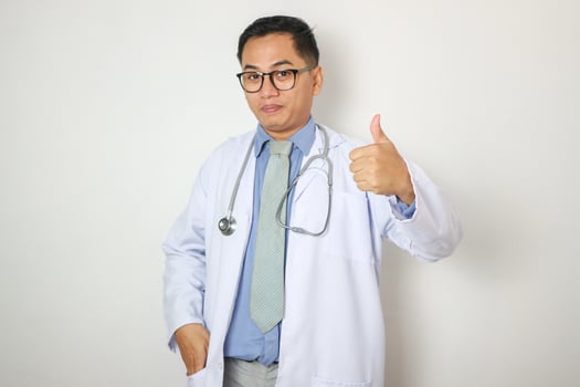 medicine, profession and healthcare concept - smiling indian male doctor in white coat with stethoscope showing thumbs up over white background photo