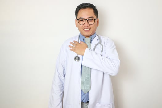 Smiling honest asian male nurse or doctor, intern in scrubs giving pledge, raising one arm and hold hand on heart while promise, oath to patient over white background photo