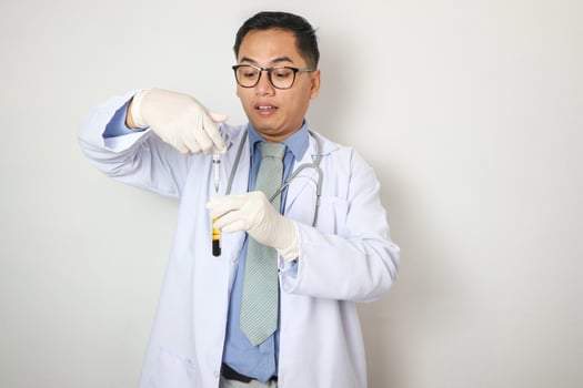 Young male Asian scientist or researcher is using syringe for collect a blood of patient to blood sample tube in medical research room. Medical researcher concept. photo