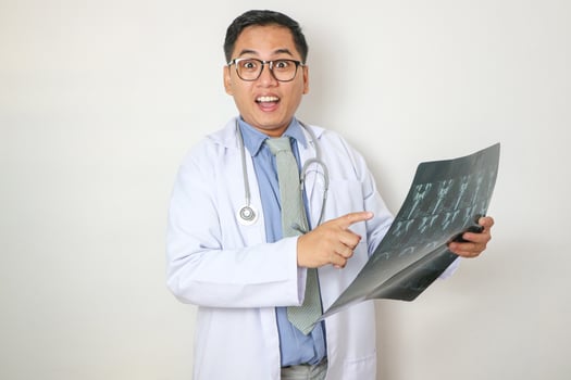 Young Asian male doctor exam x-ray film lung in clinic. radiologist analyzing the results and recording the information on laptop computer in hospital lab. concept Medical consultation, health care photo