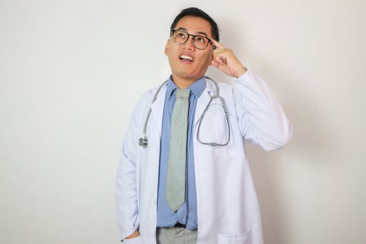 Pensive young chinese guy therapist in white coat and glasses thinks and looks at free space, isolated on white background, studio. Doctor choice, idea and solution for treatment, medical health care photo