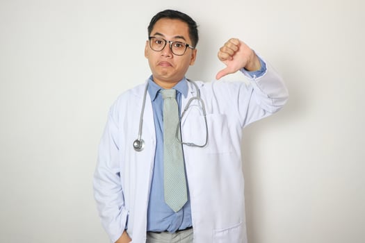 Young Chinese man as a medical doctor in studio showing a dislike gesture, thumbs down. Disagreement concept. photo