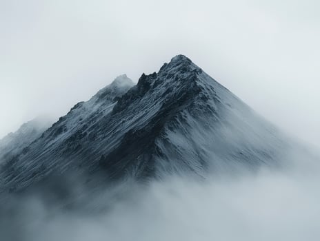 In a realm where mist dances with stone, behold the ethereal embrace of fog-veiled mountains Jagged peaks emerge like ancient sentinels, their rugged forms softened by the delicate touch of swirling photo