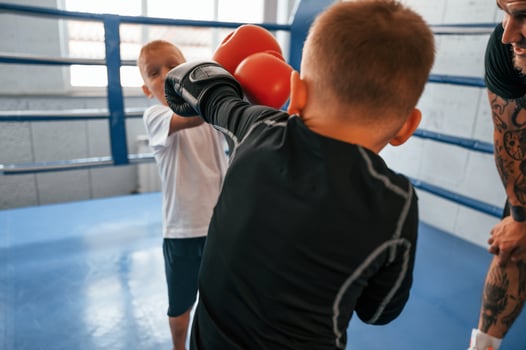 Fighting on the ring. Young tattooed coach teaching the kids boxing techniques., photo
