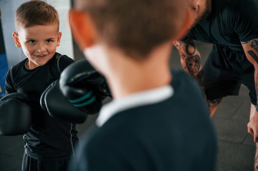 Having fun by practicing. Young tattooed coach teaching the kids boxing techniques.. photo