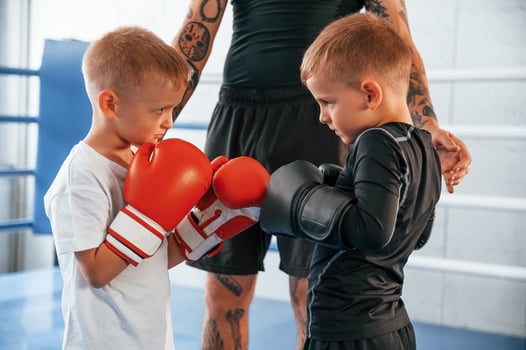 Opponents looking in each other's eyes before the round starts. Young tattooed coach teaching the kids boxing techniques, photo