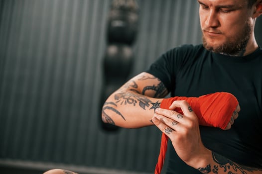 Almost ready.. Wearing hand wraps. Young tattooed man is practicing boxing indoors in the gym. photo