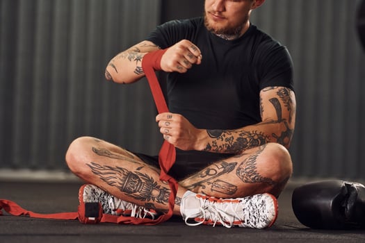 Wearing hand wraps. Young tattooed man is practicing boxing indoors in the gym. photo