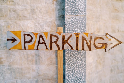 Wooden pointer with an arrow near the stone wall. Caption. Parking photo