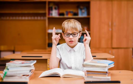 Emotional cute boy in glasses and a white shirt at a school desk with textbooks photo