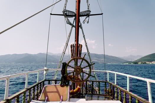 Steering wheel of a wooden schooner near a mast with a mars platform floating on the sea photo