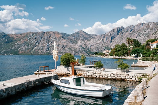 Small boat is moored at the stone pier of an ancient town at the foot of the mountains. Dobrota, Montenegro photo