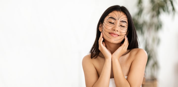 Asian woman is pampering herself with a skincare treatment, smiling contentedly while getting a facial massage. She is in a bright, serene skincare studio designed for relaxation and rejuvenation. photo