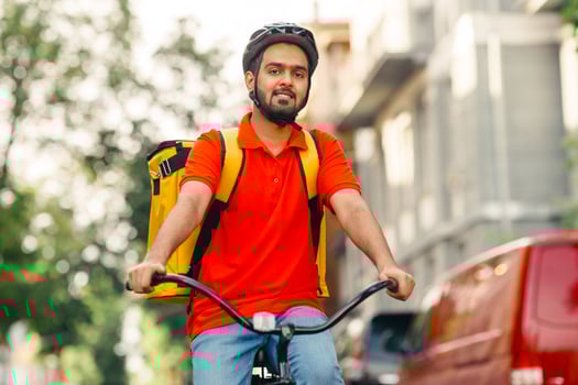 Search for delivery address. Courier in helmet with yellow backpack rides a bicycle down the street, free space photo