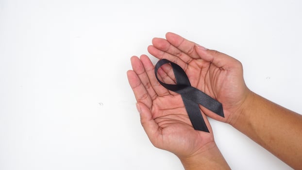 Man hands holding black ribbon as symbol of mourning and melanoma cancer awareness isolated on white background photo