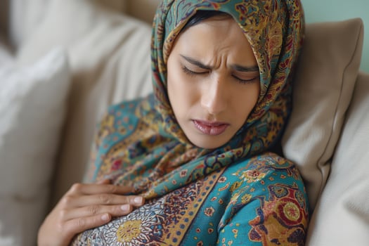 A young Middle-Eastern woman wearing a colorful scarf looks distressed while resting on a couch, conveying a sense of discomfort. photo