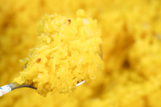 Yellow rice scooped from a spoon against a bright backdrop photo