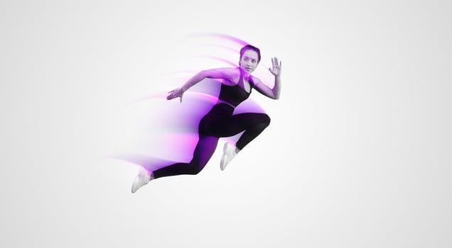 A woman wearing a black top and black leggings is captured mid-jump in the air. Her arms are outstretched and her legs are bent, showcasing her athleticism and agility as she defies gravity. photo