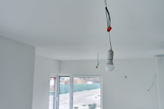 Single light bulb hanging from exposed electrical wires in unfinished interior with white walls and concrete flooring. Lighting in building under renovation photo