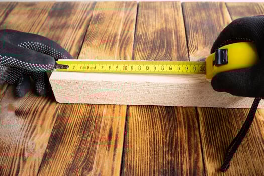 Male hand measuring piece of wood with yellow measuring tape in carpentry photo