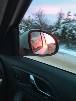 A car skillfully maneuvers along a slippery snowy road while a breathtakingly stunning sunset casts its warm, golden light over the calm and peaceful winter landscape all around photo