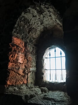 A weathered stone wall features a barred window, highlighting its ancient structure and the impact of time. This site evokes a sense of history, echoing stories of the past photo