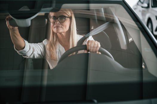 Front view. Woman in white formal clothes is in the car dealership photo