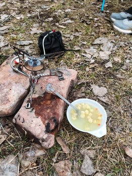 A beautifully crafted bowl filled with warm, delicious soup is resting on a large rock, which is conveniently located right beside a stove that is actively being used for cooking photo