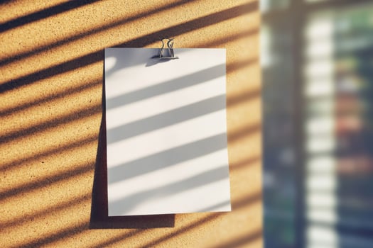 Blank white paper on corkboard with sunlight casting striped shadows photo