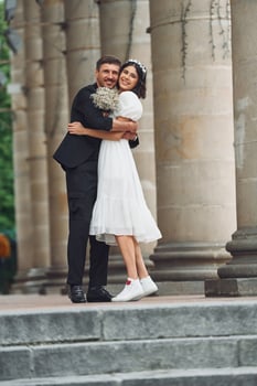 Standing and posing near building. Beautiful bride with his fiance is celebrating wedding outdoors. photo