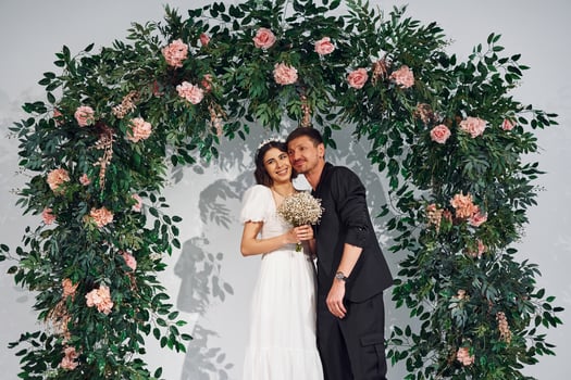 Standing against flowers. Beautiful bride with his fiance is on the wedding photo