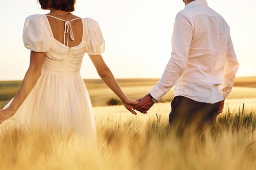 Walking and holding each other by the hand.s. Couple just married. Together on the majestic agricultural field at sunny day photo