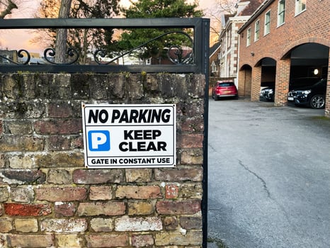 No parking sign on brick wall near driveway with evening setting photo