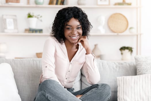 Happy African American Girl Posing In Stylish Living Room Interior, Smiling At Camera While Sitting On Comfortable Couch photo