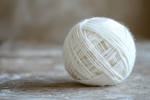 White ball of yarn resting on a rustic wooden surface with soft natural lighting photo
