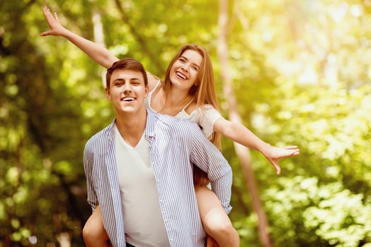 Loving couple having fun together at park, boyfriend giving piggyback ride to his girlfriend. Copy space photo