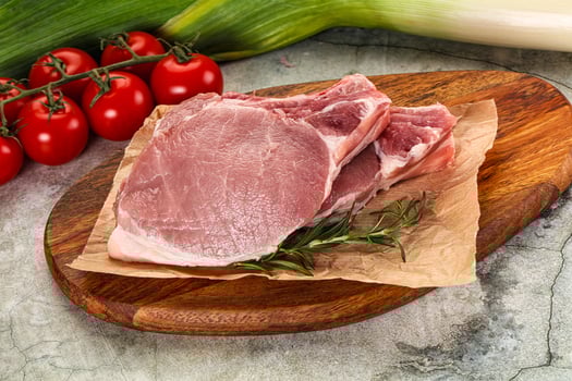 Raw pork on a wooden cutting board with tomatoes and herbs photo