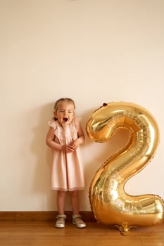 Little laughing girl stands against the wall near the inflatable golden number two photo