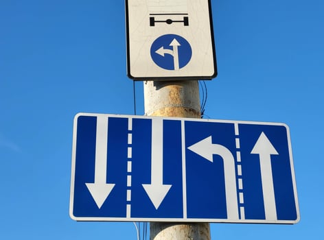 White arrows on a blue background are a standard road sign on a vertical pole against the sky photo