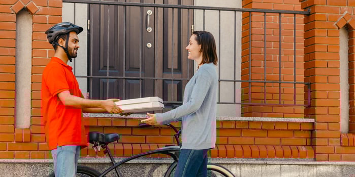 Ecological city, bike and delivering service. Smiling courier in helmet gives pizza to client, near entrance, at street, side view, free space photo